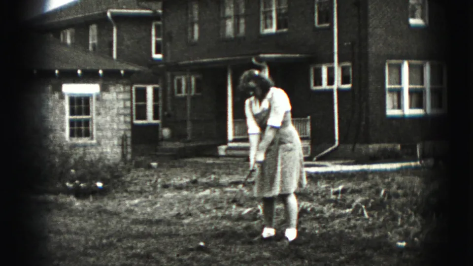 A wider 1975 Harrisburg frame shows the woman using a golf club in a yard beside neighboring residential buildings.