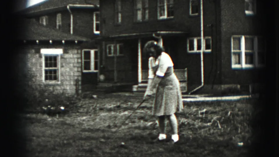 In Harrisburg, Pennsylvania home-movie footage from 1975, a woman prepares a golf shot in a backyard near a brick house.