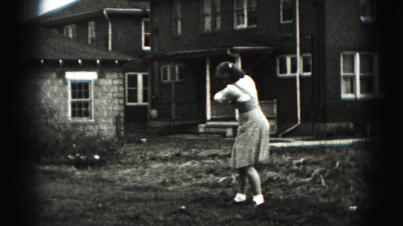 Woman follows through on a golf swing in front of a house.