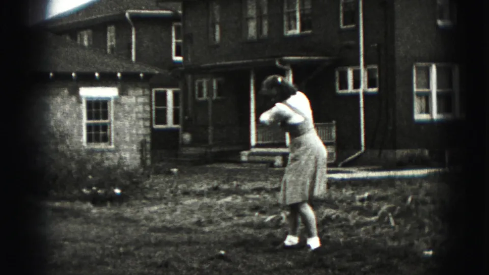 The woman swings a golf club in a residential yard, with porch steps and house windows behind her.