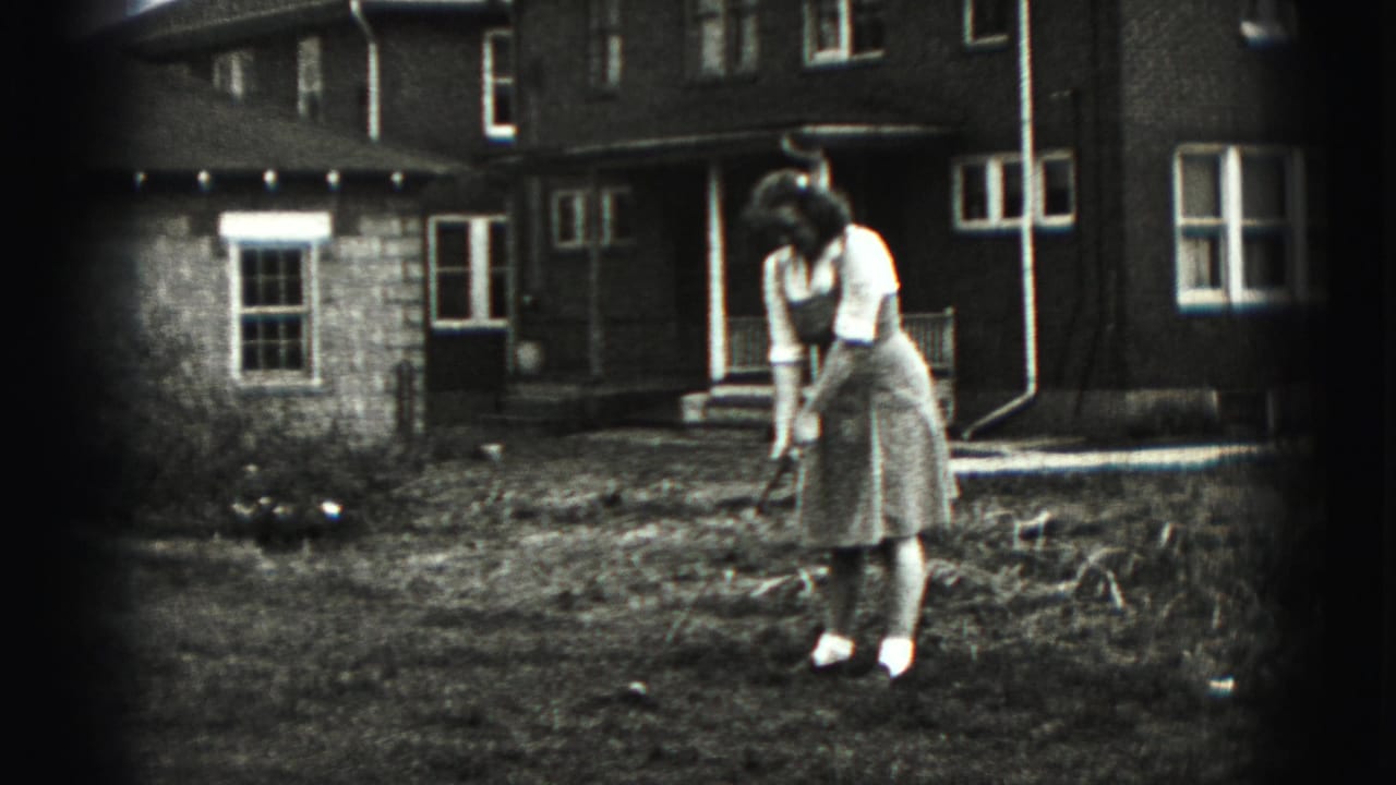 Woman in a light dress stands in a yard with a golf club in front of a house.
