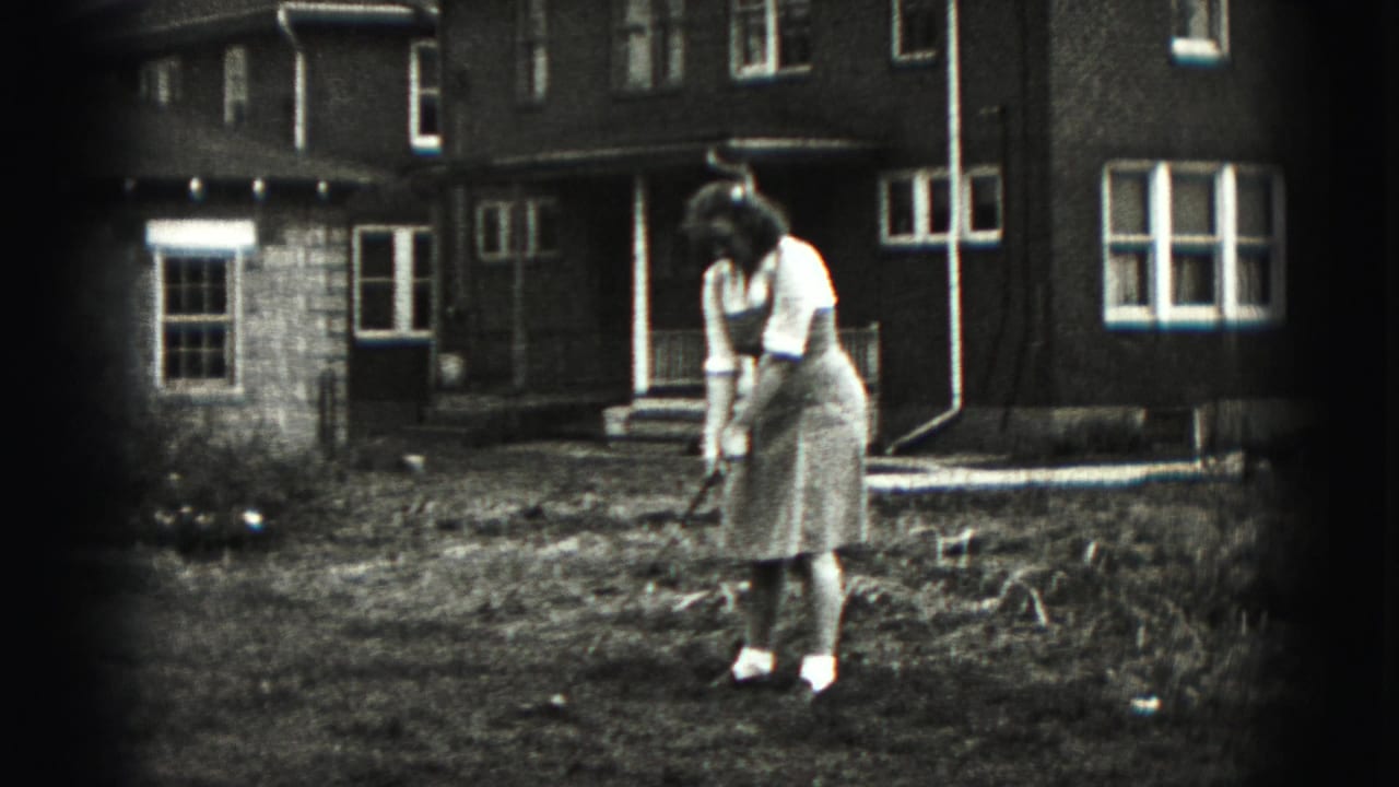 The woman remains focused on the golf ball or ground target while standing outside a Harrisburg house in 1975 footage.