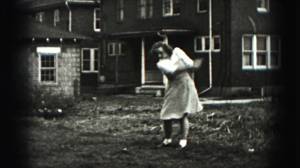 The woman completes her golf swing in a residential yard in the Harrisburg 1975 home-movie clip.