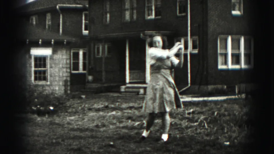 In a Harrisburg, Pennsylvania 1975 home-movie frame, a woman practices a golf swing in a yard outside a brick house.
