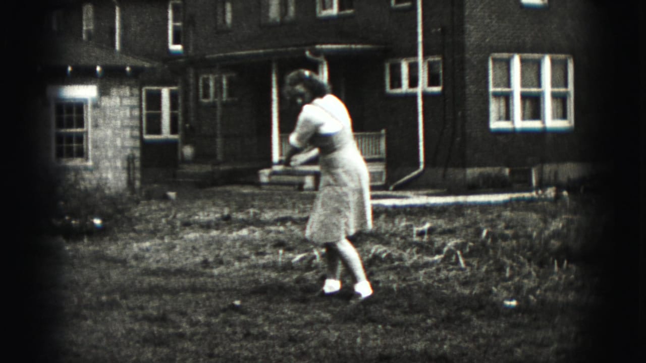 A woman follows through on a golf swing in a suburban backyard in the Harrisburg, Pennsylvania home-movie footage.