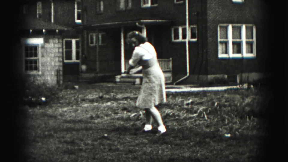 A woman follows through on a golf swing in a suburban backyard in the Harrisburg, Pennsylvania home-movie footage.