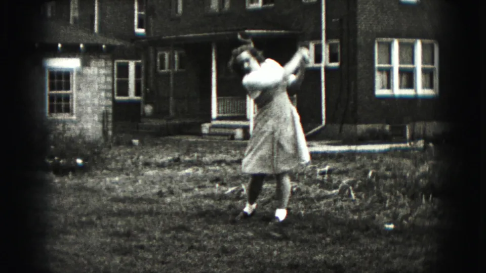 The woman is seen mid-swing or follow-through with a golf club in the 1975 Harrisburg backyard scene.