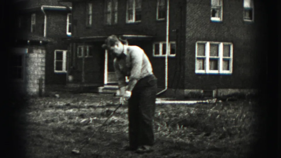 A man in a collared shirt and dark pants prepares or finishes a golf swing in the Harrisburg backyard home movie.