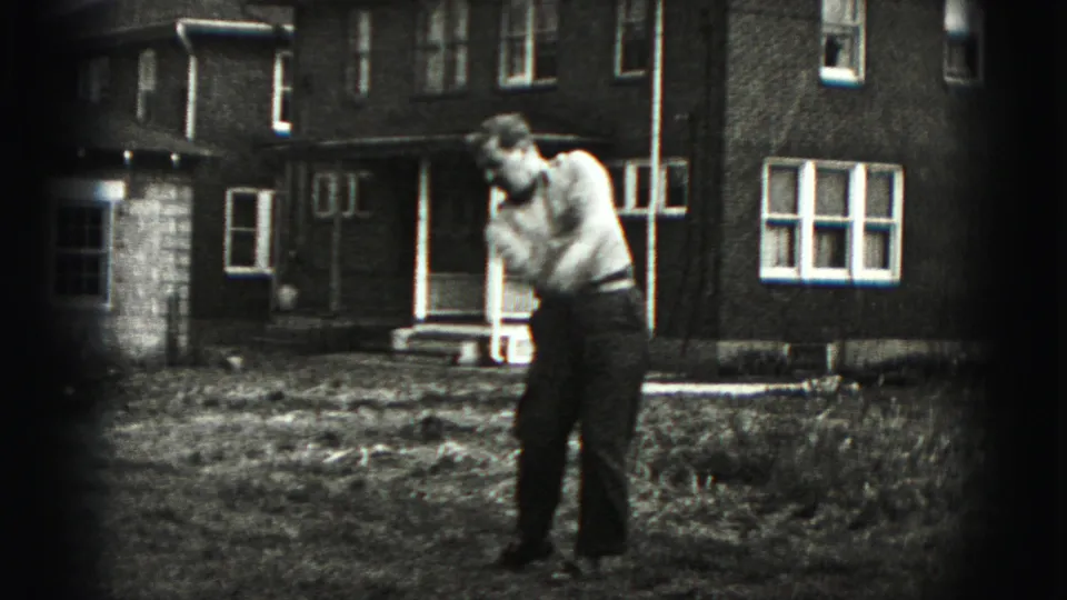 The man completes a golf swing in the Harrisburg yard, his club raised as the brick house and porch stay in the background.