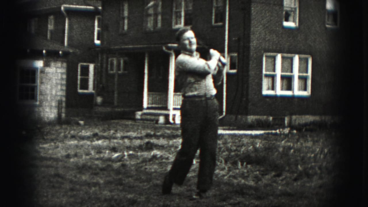 In 1975 Harrisburg home-movie footage, a man stands in a grassy yard with a golf club raised during a practice swing.