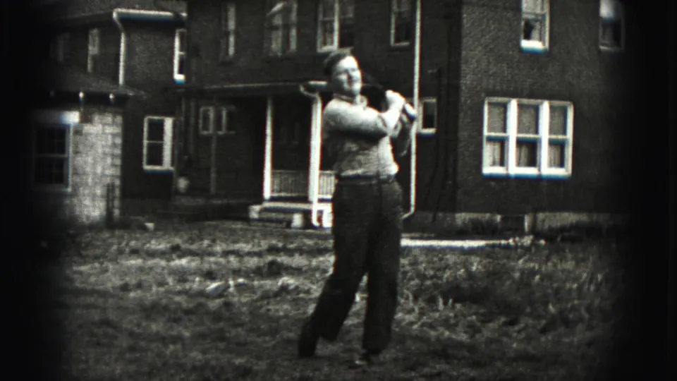In 1975 Harrisburg home-movie footage, a man stands in a grassy yard with a golf club raised during a practice swing.