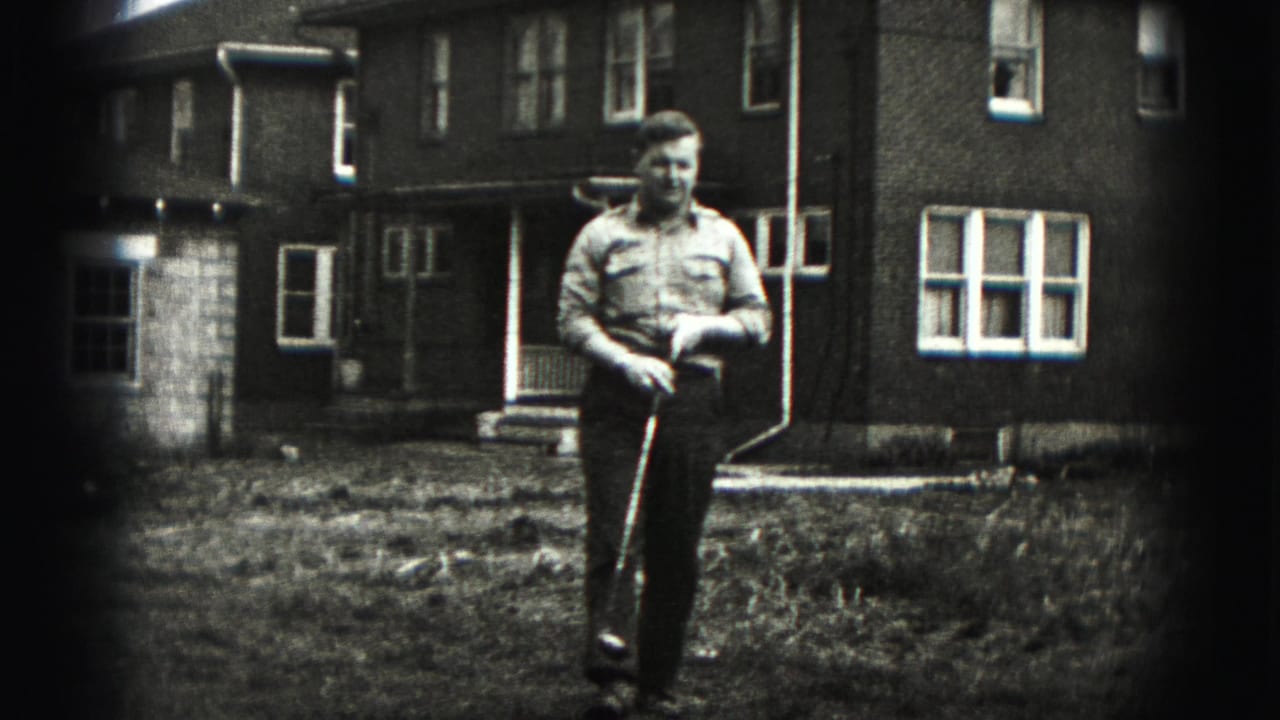 Man walks forward holding a golf club in front of a brick residential building.
