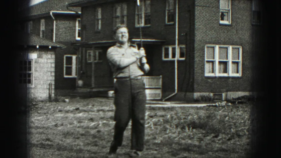 After the swing, the man stands with the club in a grassy yard outside a Harrisburg brick house.