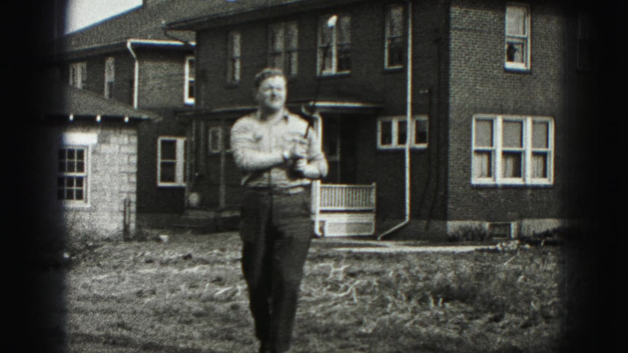 Man holding a golf club in a grassy yard before a brick house.
