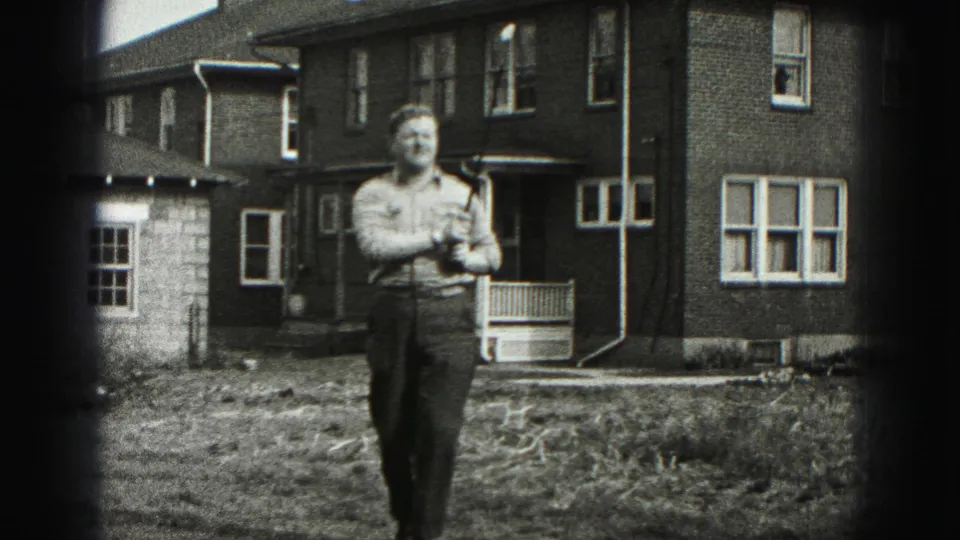 In Harrisburg home-movie footage from 1975, a man stands in a yard holding a golf club in front of a brick residence.