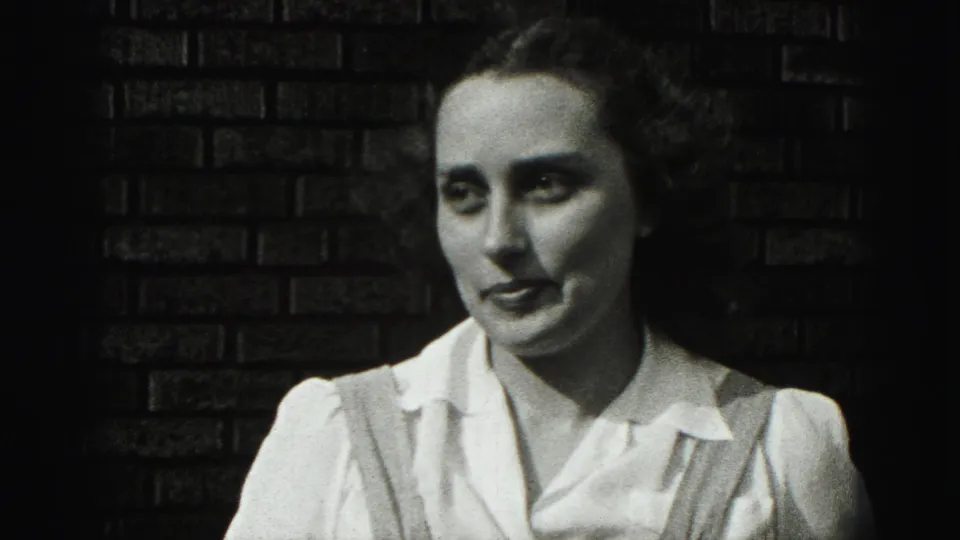 A young woman in a white blouse and suspenders faces the camera against a brick wall in Harrisburg, Pennsylvania, 1975.