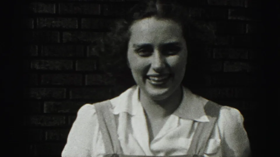 The woman laughs more broadly in the close Harrisburg home-movie portrait, with her blouse and overall straps visible against the wall.