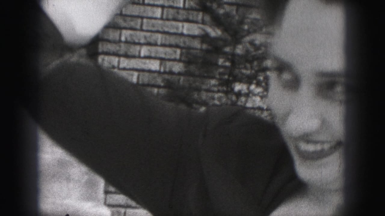 The woman turns partly in profile and smiles, her arm raised as she adjusts her hair against the brick-wall background.