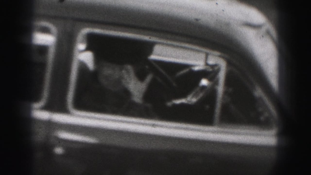 Passenger inside a dark car raises a hand near the side window.
