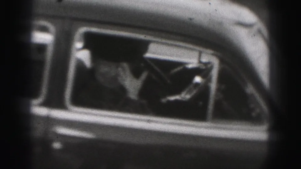 1975 Harrisburg home-movie frame with a person waving from the side window of a dark car.