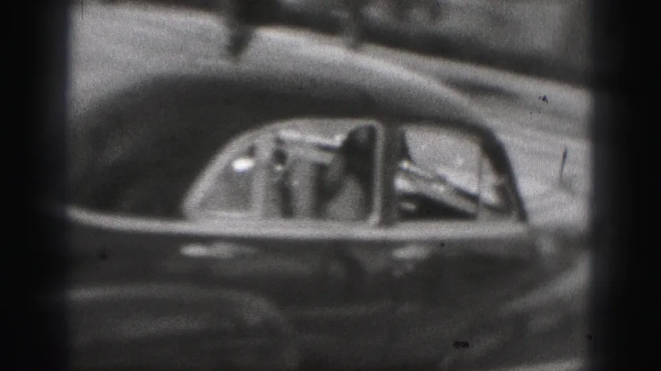 1975 Harrisburg 8mm frame showing a dark car passing with a passenger visible through the side window.