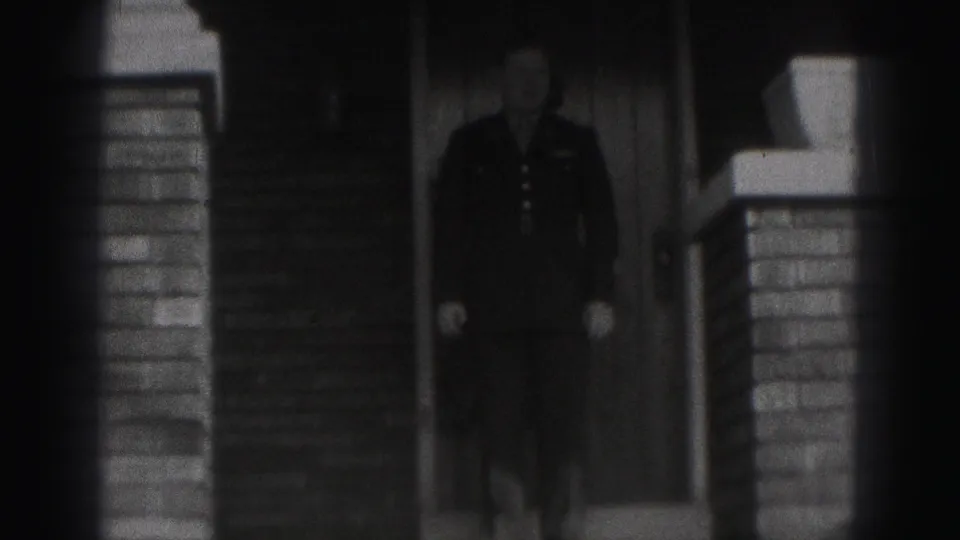 A man in formal clothing appears on exterior steps beside brick porch columns in 1975 Harrisburg footage.