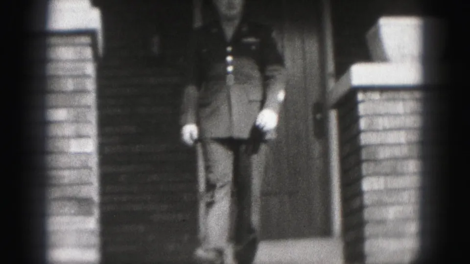 A suited man descends exterior steps at a brick house entrance in Harrisburg archival home-movie footage.
