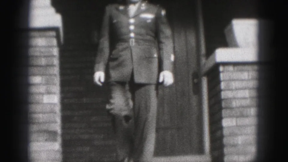 A young man in a military-style dress uniform descends the steps of a brick home in Harrisburg, Pennsylvania, in 1975 home-movie footage.