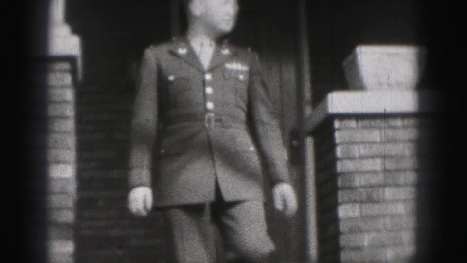 The uniformed man approaches the camera from the porch area, with brick columns and a doorway visible behind him.