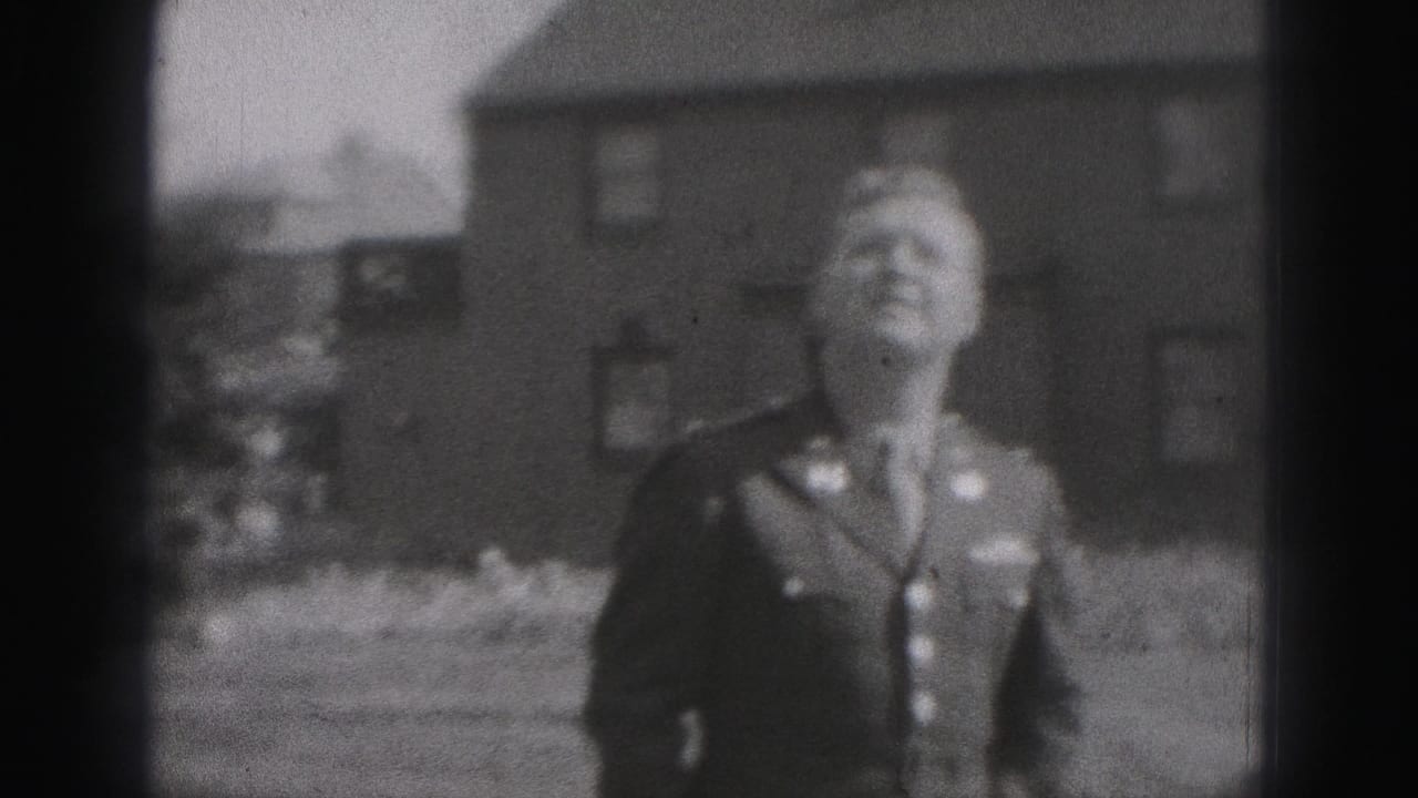 The uniformed man stands in a residential yard in Harrisburg, Pennsylvania, looking upward beside brick houses in soft 8mm footage.