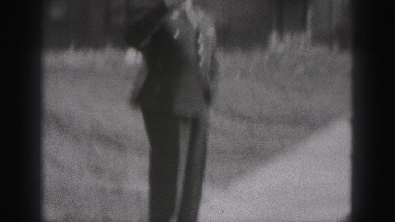 A uniformed police officer appears at a distance on a residential sidewalk in 1975 Harrisburg home-movie footage.