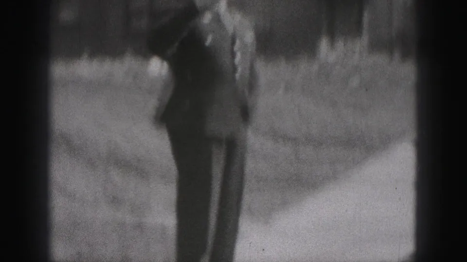 A uniformed police officer appears at a distance on a residential sidewalk in 1975 Harrisburg home-movie footage.
