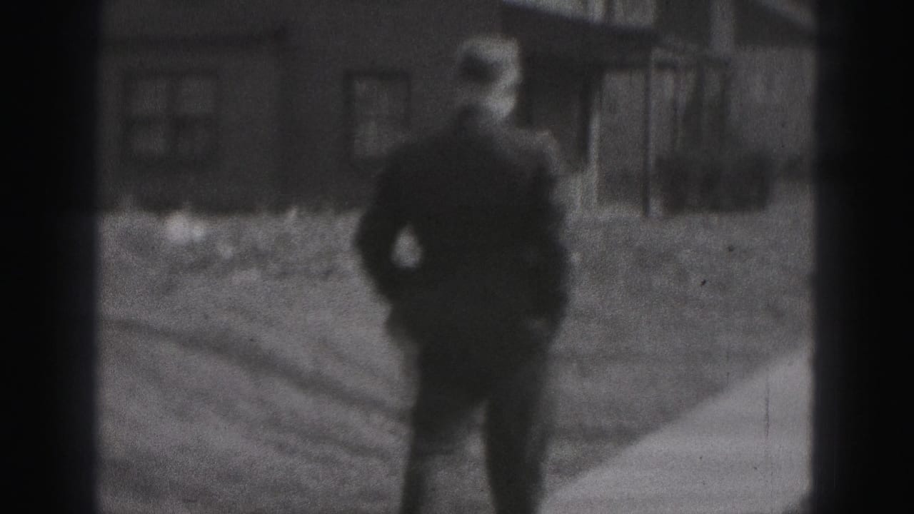 Police officer walking toward the camera on a residential sidewalk with houses behind him.