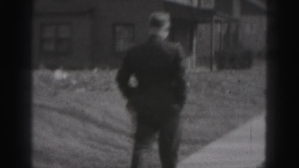 A uniformed police officer walks toward the camera on a Harrisburg residential sidewalk, with houses and yards in the background.