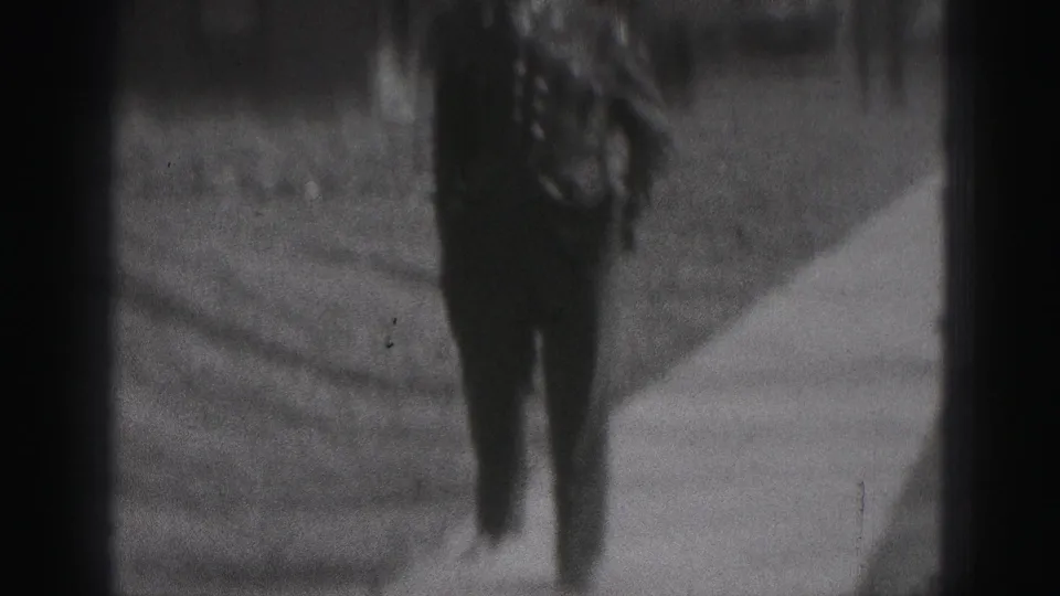 The home-movie camera catches a close, partial view of the officer's dark uniform while he passes along the sidewalk.