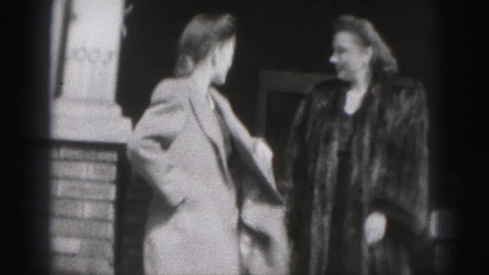 In 1975 Harrisburg home-movie footage, two women in coats appear outside a brick building entrance.
