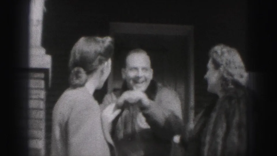 A smiling man appears to greet two women by a doorway in the 1975 Harrisburg home-movie footage.