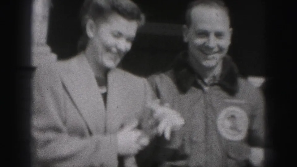A woman in a light coat smiles beside a man in a collared shirt during the Harrisburg 1975 greeting.