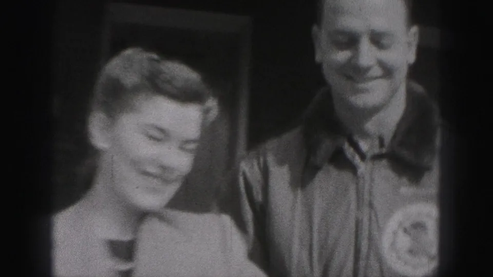 In 1975 Harrisburg home-movie footage, a woman and man smile toward the camera with soft focus and dark frame edges.