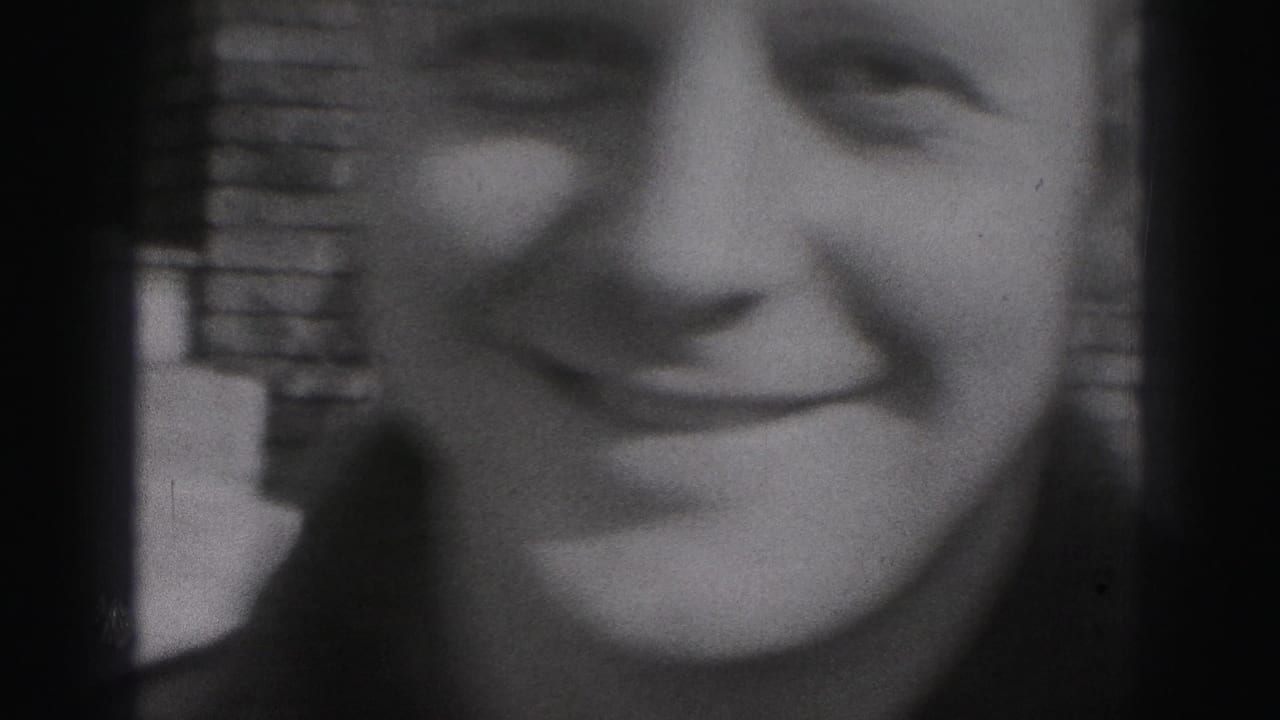 Soft close-up of part of a smiling face beside a brick wall in black-and-white film.