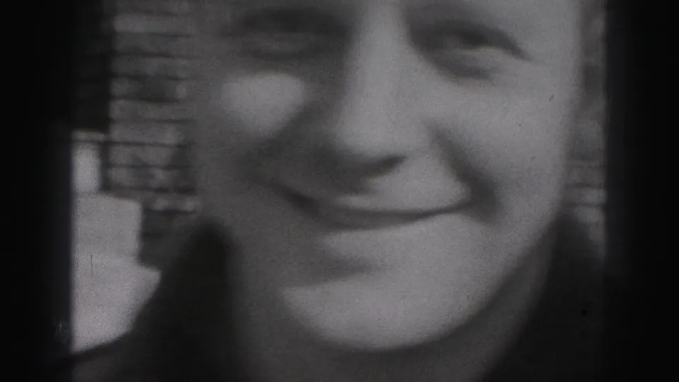 A soft, close-cropped 1975 Harrisburg home-movie frame shows part of a smiling adult face near a brick wall.