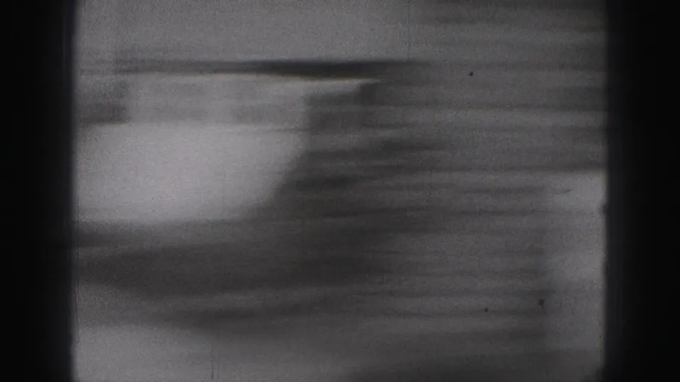 A motion-blurred 8mm frame from the 1975 Harrisburg clip shows the camera shifting away from the people toward an indistinct surface.