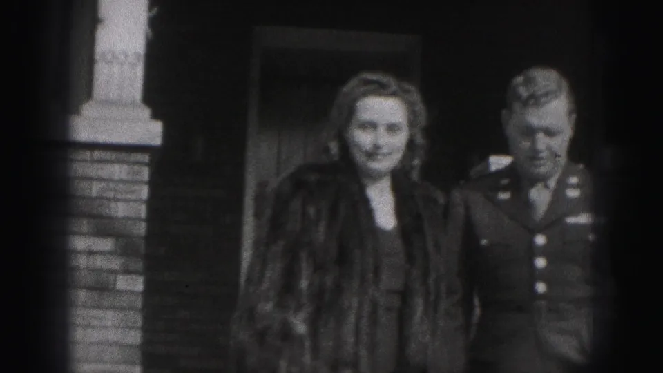 A woman in a fur coat poses beside a uniformed man near a brick building entrance in Harrisburg, 1975.