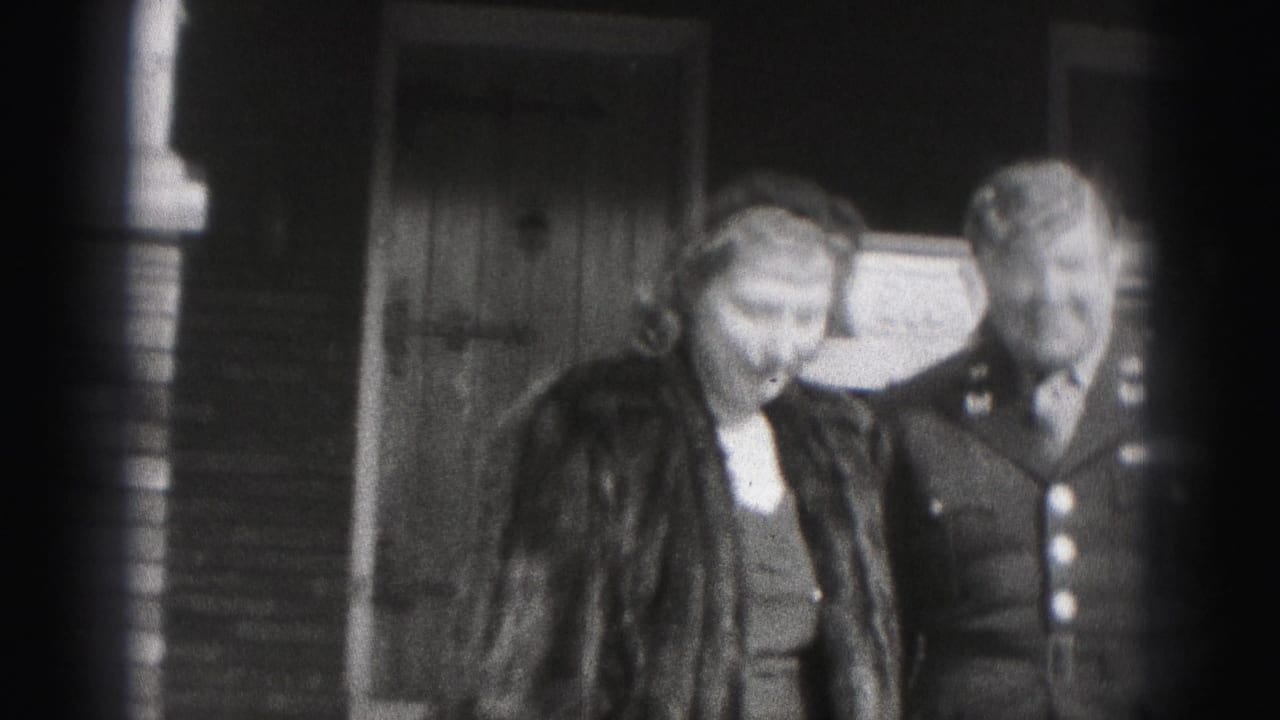 Woman in a fur coat and uniformed man standing outside a house entrance.