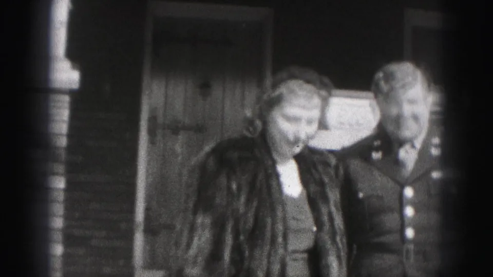 In Harrisburg, Pennsylvania, a woman in a fur coat and a man in military dress uniform stand near a house doorway in 1975 home-movie footage.