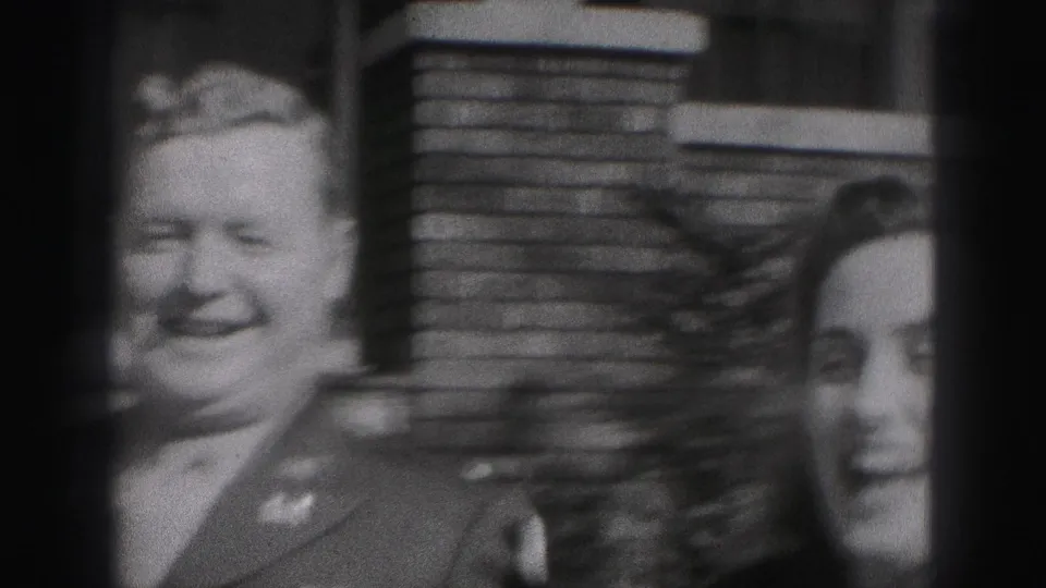 The uniformed man smiles toward the camera while the woman appears partly visible beside him outside the Harrisburg brick home.