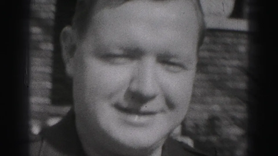 Close 1975 Harrisburg home-movie frame of the uniformed man smiling toward the camera outside a brick residence.