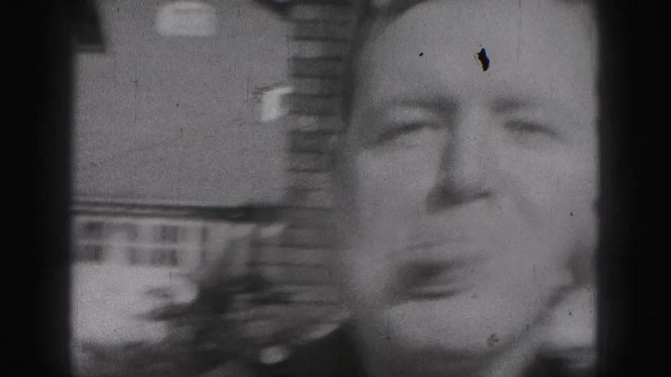 In 1975 Harrisburg home-movie footage, a uniformed man leans close to the camera and sticks out his tongue outside a brick house.