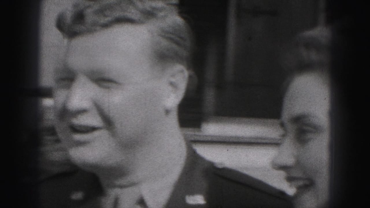 Uniformed man smiles beside a woman outside a brick house.
