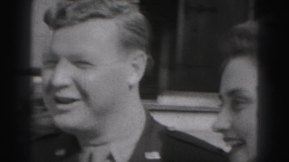 The uniformed man smiles in profile while a woman stands close beside him outside a brick residential building in Harrisburg.